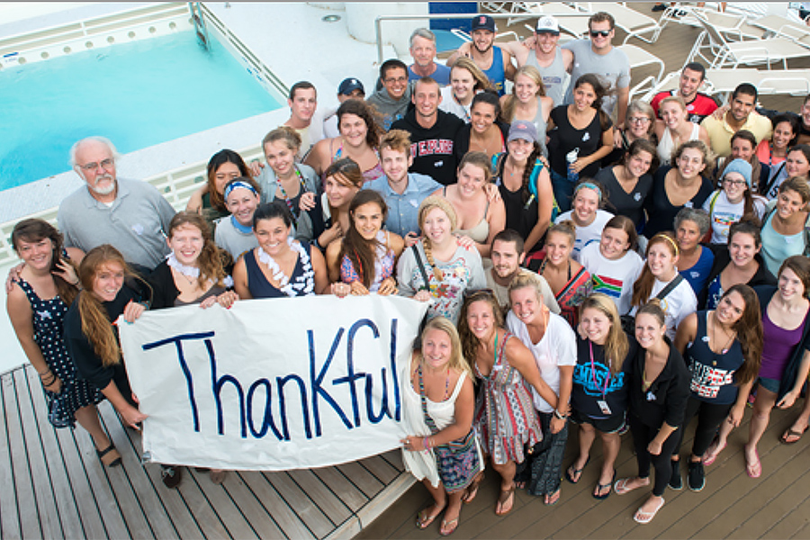 A group of students stand on the deck of a ship with a sign that says "Thankful."